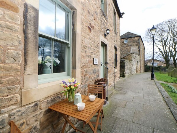 A stone building with a window, a table with a vase of flowers, and a chair.