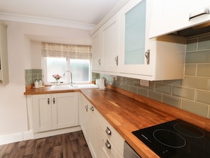 A kitchen with white cabinets, a wooden countertop, a black induction cooktop, and a window with a curtain.