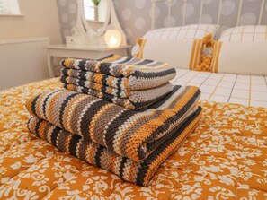 Un letto ben rifatto con una coperta a motivi e un mucchio di coperte piegate.