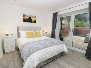 Quarto com cama, mesas de cabeceira, um criado-mudo, janela com cortinas e vista para o exterior.