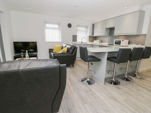 A modern living room with a sofa, a TV, and a dining area with a kitchen in the background. - Contemporary Apartment 1 in Whitby (Whitby)