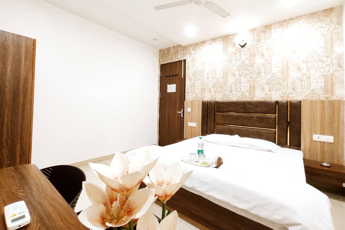 A hotel room with a bed, a desk, a chair, a ceiling fan, and a wall with patterned wallpaper.