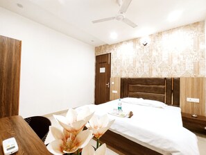 A hotel room with a bed, a desk, a chair, a ceiling fan, and a wall with patterned wallpaper.