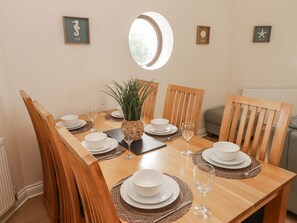 A dining table set with white plates, bowls, and wine glasses, surrounded by wooden chairs. - Awel y Môr, Burry Port (Burry Port)