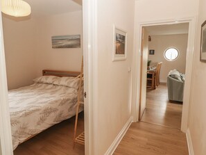 Un dormitorio con una cama, una mesita y una silla. Hay una puerta que da a otra habitación.