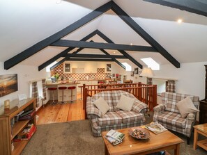 A loft-style room with exposed beams, a kitchen in the background, and a cozy seating area with plaid sofas. - The Haven is in Northumberland (Berwick-upon-Tweed)