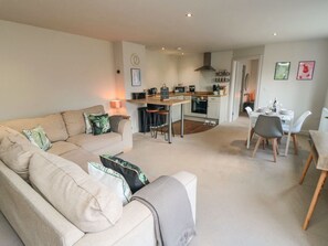 A living room with a sofa, a dining table with chairs, a kitchen area with a stove and microwave, and a hallway leading to another room. - The Annexe, Bridlington, North Yorkshire. (Bridlington)