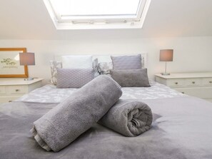 A bedroom with a skylight, a bed with rolled towels, two bedside tables with lamps, and a framed picture on the wall. - Acorn Cottage is in Windermere (Windermere)
