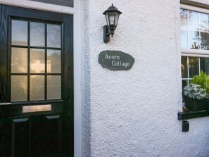 A cottage with a black door, a white wall, a lantern, and a sign that reads 'Acorn Cottage.' - Acorn Cottage is in Windermere (Windermere)