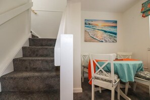 Eine Treppe führt zu einem Raum mit einem Gemälde von einer Strandansicht, einem Tisch mit Stühlen und einem weißen Geländer.