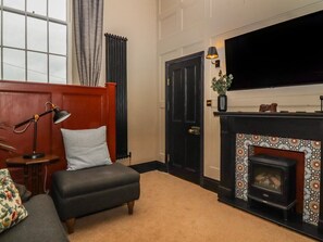 A living room with a sofa, a lamp, a fireplace, a TV, and a door. - The Court, Ingleton, Yorkshire (Carnforth)