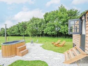 Une cabane en bois avec un jacuzzi, une terrasse en bois et un fauteuil de relaxation.