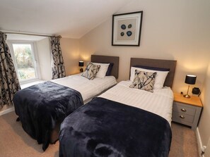 A double room with two beds, a window with curtains, a bedside table with a lamp, and a framed picture on the wall. - The Cottage, Tetbury (Tetbury)