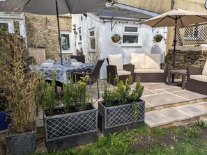 An outdoor patio with wicker furniture, a table set for dining, and potted plants. - The Cottage, Tetbury (Tetbury)