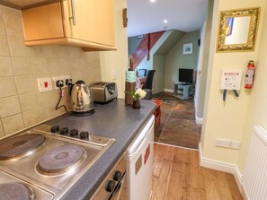 Eine Küche mit Herd, Wasserkocher und Toaster, ein Essbereich mit Tisch und Stühlen sowie ein Wohnzimmer mit Fernseher.