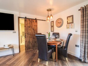 A dining area with a wooden table, black chairs, a clock, and a sliding barn door. - Blockley Lodge, Wall-Under-Heywood (Church Stretton)
