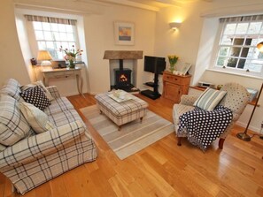 A cozy living room with a fireplace, a sofa, a chair, and a small table. - Sunrise Cottage, Padstow (Padstow)