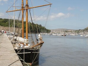 A docked sailing ship with masts and rigging, surrounded by calm water and a marina with other boats. - Elsinore in Conwy, North Wales (Conwy)