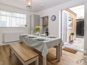 A dining area with a table set for four, a clock on the wall, and a view of the outside. - Elsinore in Conwy, North Wales (Conwy)