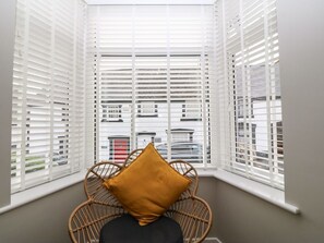 A corner room with white blinds, a wicker chair, and a black cushion. - Elsinore in Conwy, North Wales (Conwy)