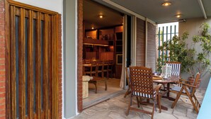 A patio area with a table and chairs, a brick wall, and a wooden door. - Retro house (Rafina)