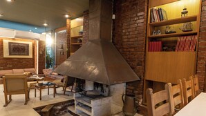 A brick fireplace with a metal vent, a wooden bookshelf with books and decorative items, a dining table with chairs, and a cushioned seating area. - Retro house (Rafina)