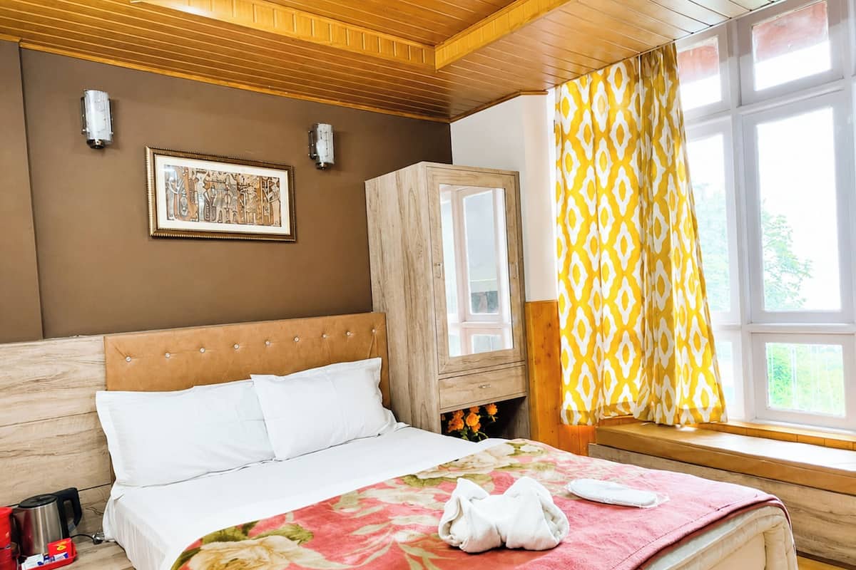 A bedroom with a bed, a wooden headboard, a nightstand, a wardrobe, a window with curtains, and a wall-mounted picture.