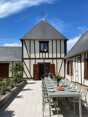 A traditional half-timbered building with a dining area set up outside, featuring a long table with chairs and a vase of flowers.