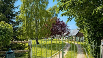 A gated entrance to a park with a gravel path, trees, and a bench.
