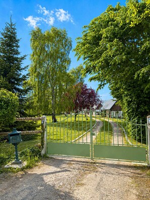A gated entrance to a park with a gravel path, trees, and a bench.
