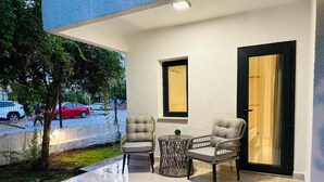 An outdoor seating area with two cushioned chairs and a small table, a door, and a window.