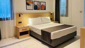 A modern hotel room with a large bed, bedside tables, an air conditioning unit, and abstract artwork on the wall.