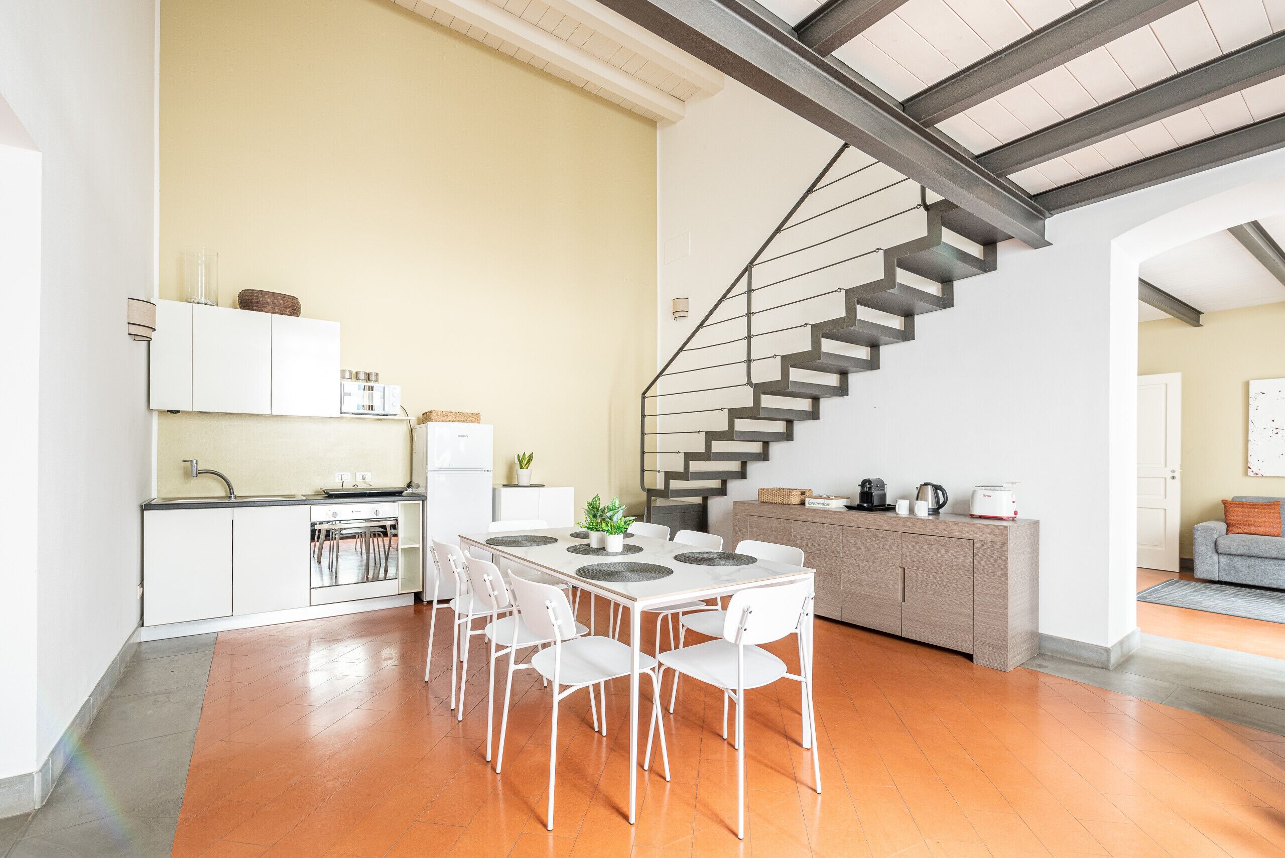 Une cuisine moderne avec des meubles blancs, une table à manger avec des chaises et un escalier.