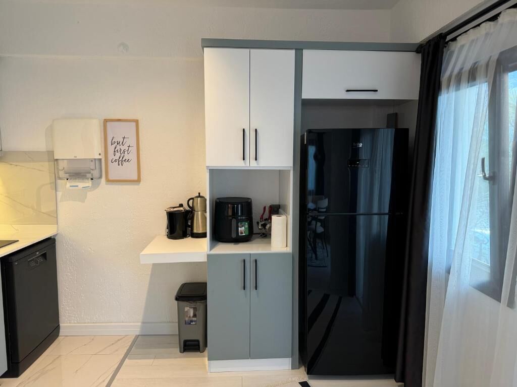 A modern kitchen with a dishwasher, a coffee machine, a refrigerator, and a small trash bin.