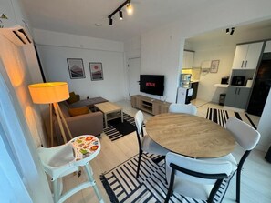 A modern living room with a TV, dining table, chairs, and a baby high chair.