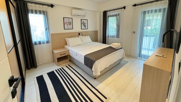 A modern hotel room with a large bed, a bedside table, a desk, and a view of the outdoors. - ORANGE SUİTE 2+1 Family Apartment - 200m Walking Distance to the Beach (Kemer)