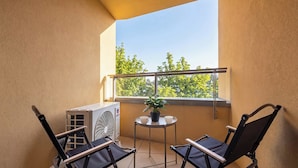 Un balcon avec deux chaises pliantes, une petite table sur laquelle est posée une plante en pot et un appareil de climatisation.