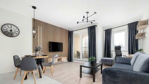 Un salon moderne comprenant un canapé, une table à manger, des chaises, un téléviseur et un mur recouvert de panneaux en bois.