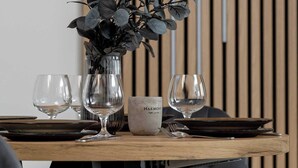 Une table à manger ornée d’un vase rempli de feuilles vertes, de verres à vin et d’une assiette.