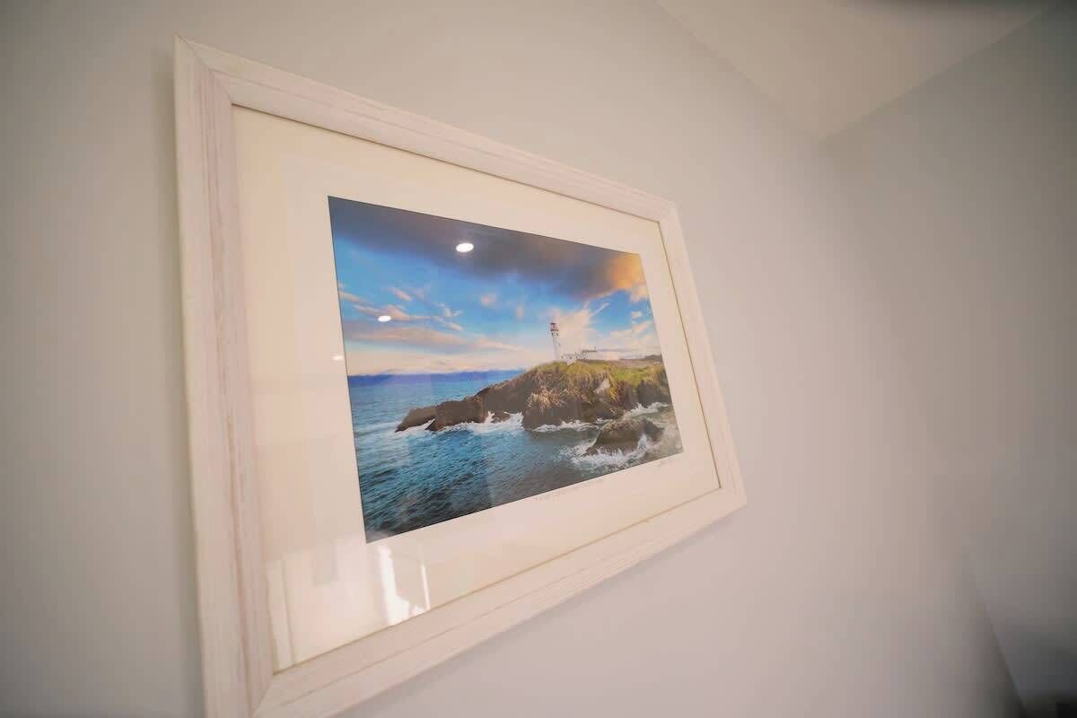 A framed photograph of a coastal scene with a lighthouse, waves, and a clear sky.
