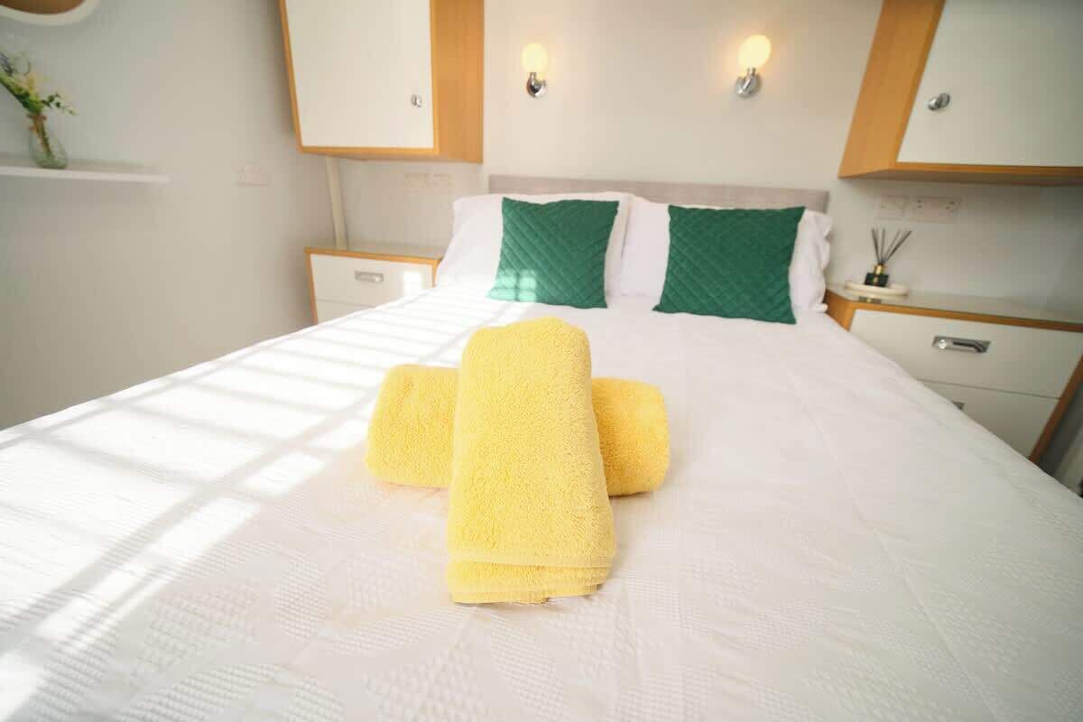 A hotel room with a bed, pillows, a nightstand, a drawer, and a wall-mounted light fixture.