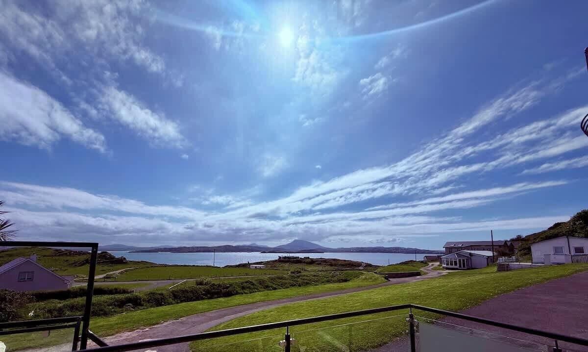 A coastal landscape with a clear sky, a distant mountain, and a small building.