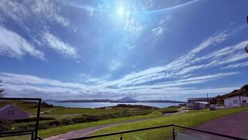 A coastal landscape with a clear sky, a distant mountain, and a small building.