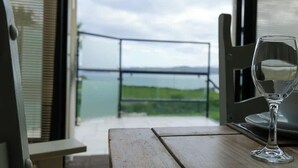 A table with a glass of water and a view of a balcony with a railing. - Atlantic View Retreat (Sleeps 6,Pet Friendly,Wifi) (Downings)