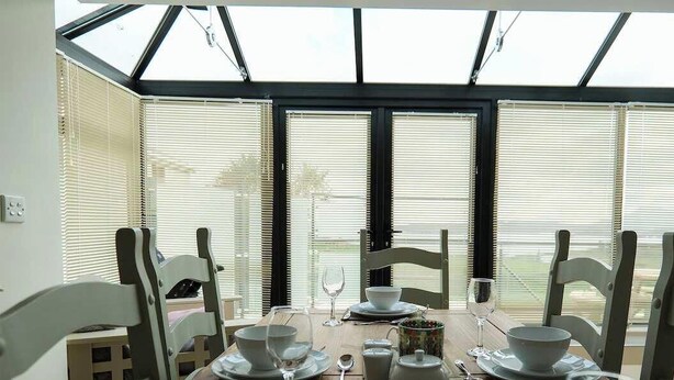 A dining table set for four with chairs, a window with blinds, and a view outside. - Atlantic View Retreat (Sleeps 6,Pet Friendly,Wifi) (Downings)