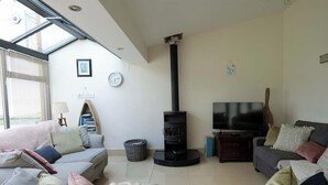 A living room with a fireplace, sofas, a television, and a window with blinds. - Atlantic View Retreat (Sleeps 6,Pet Friendly,Wifi) (Downings)