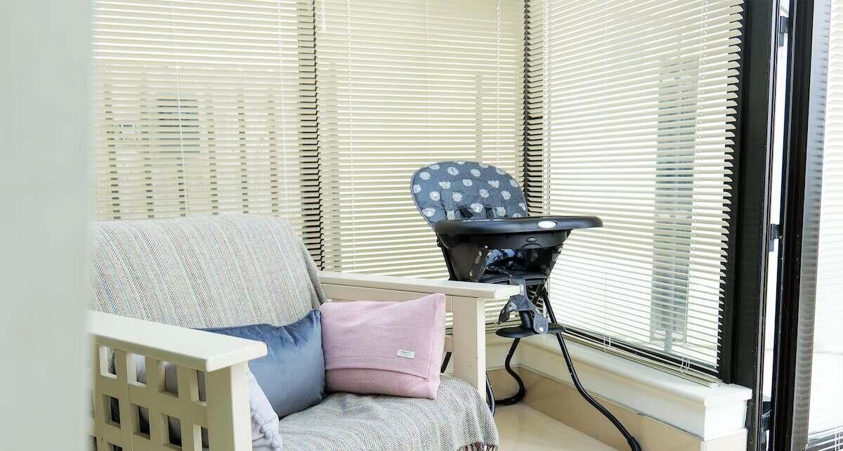 A room with a window, a chair, a baby rocker, and a crib.