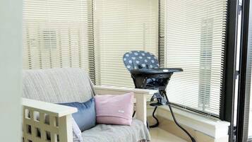 A room with a window, a chair, a baby rocker, and a crib.