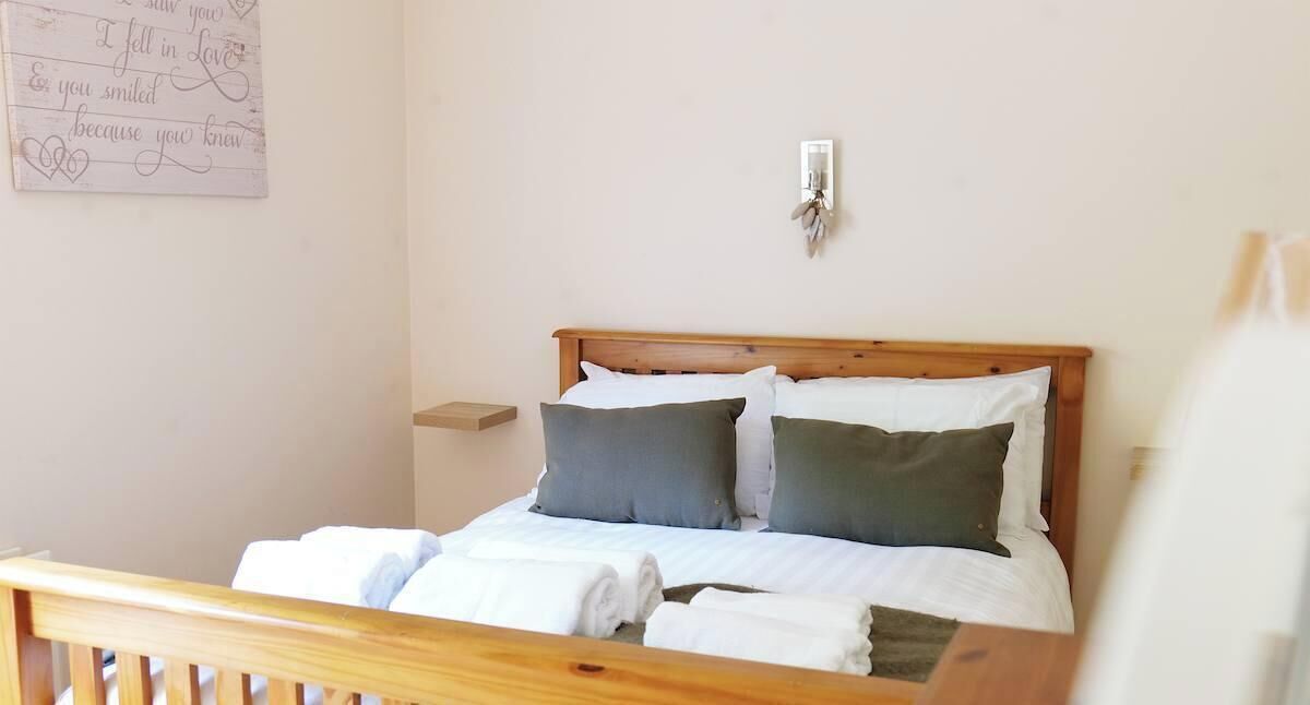 A neatly made bed with white and green bedding, a wooden headboard, a bedside table, and a wall-mounted light fixture.