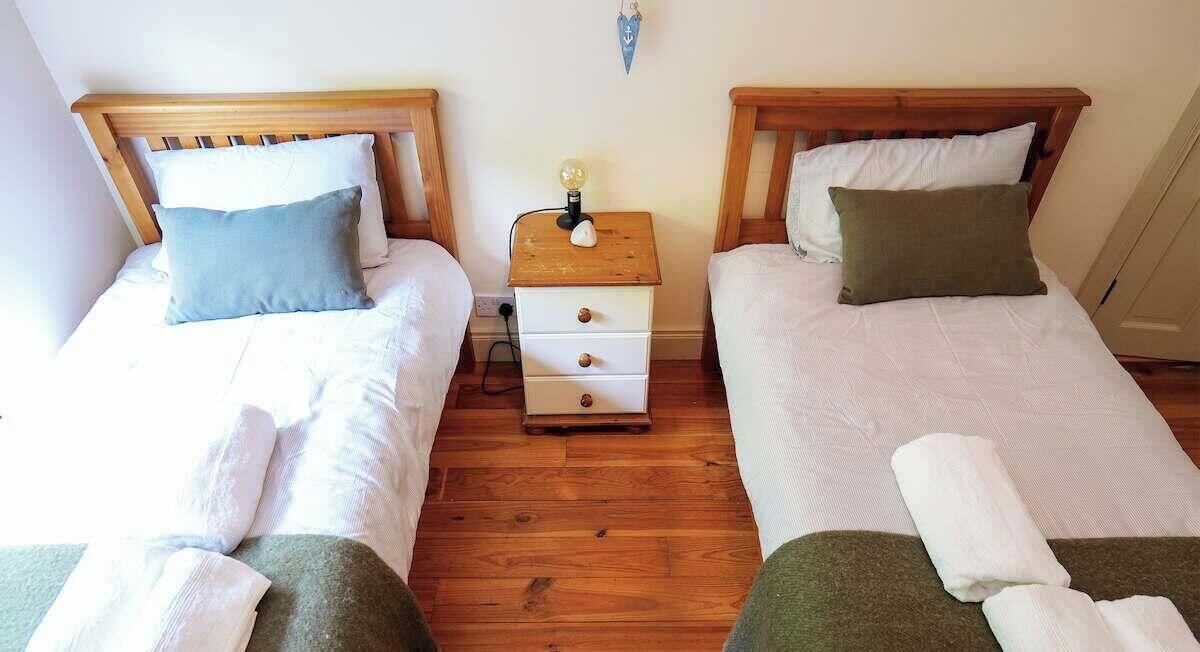 A room with two single beds, a wooden nightstand with a lamp, and a wall-mounted light fixture.